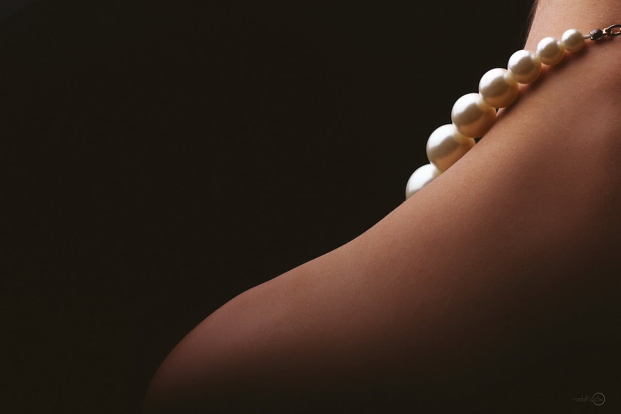 Elegant close-up of a woman's bare shoulder adorned with a pearl necklace, set against a dark background.