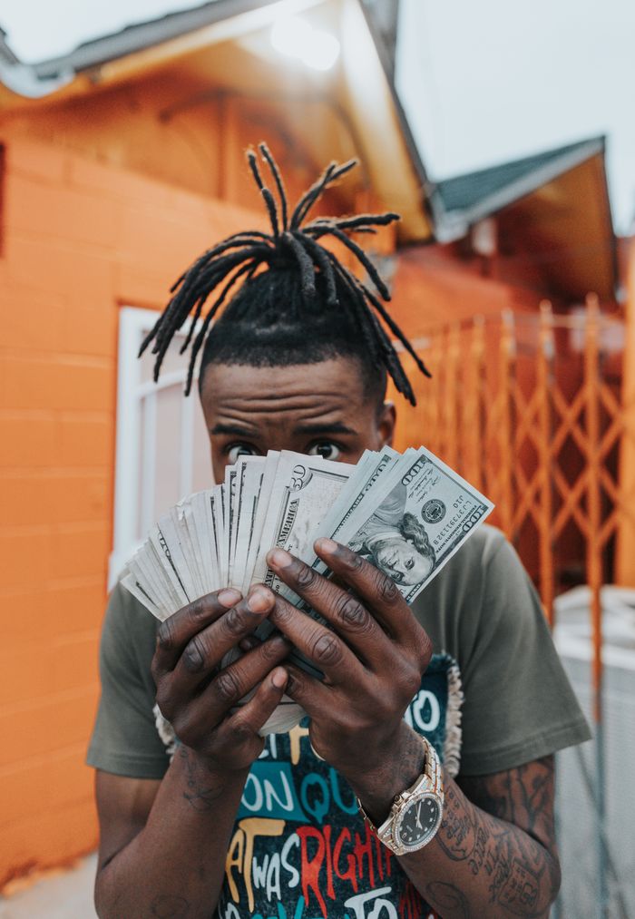 A young man holding a stack of dollar bills in front of a colorful building.